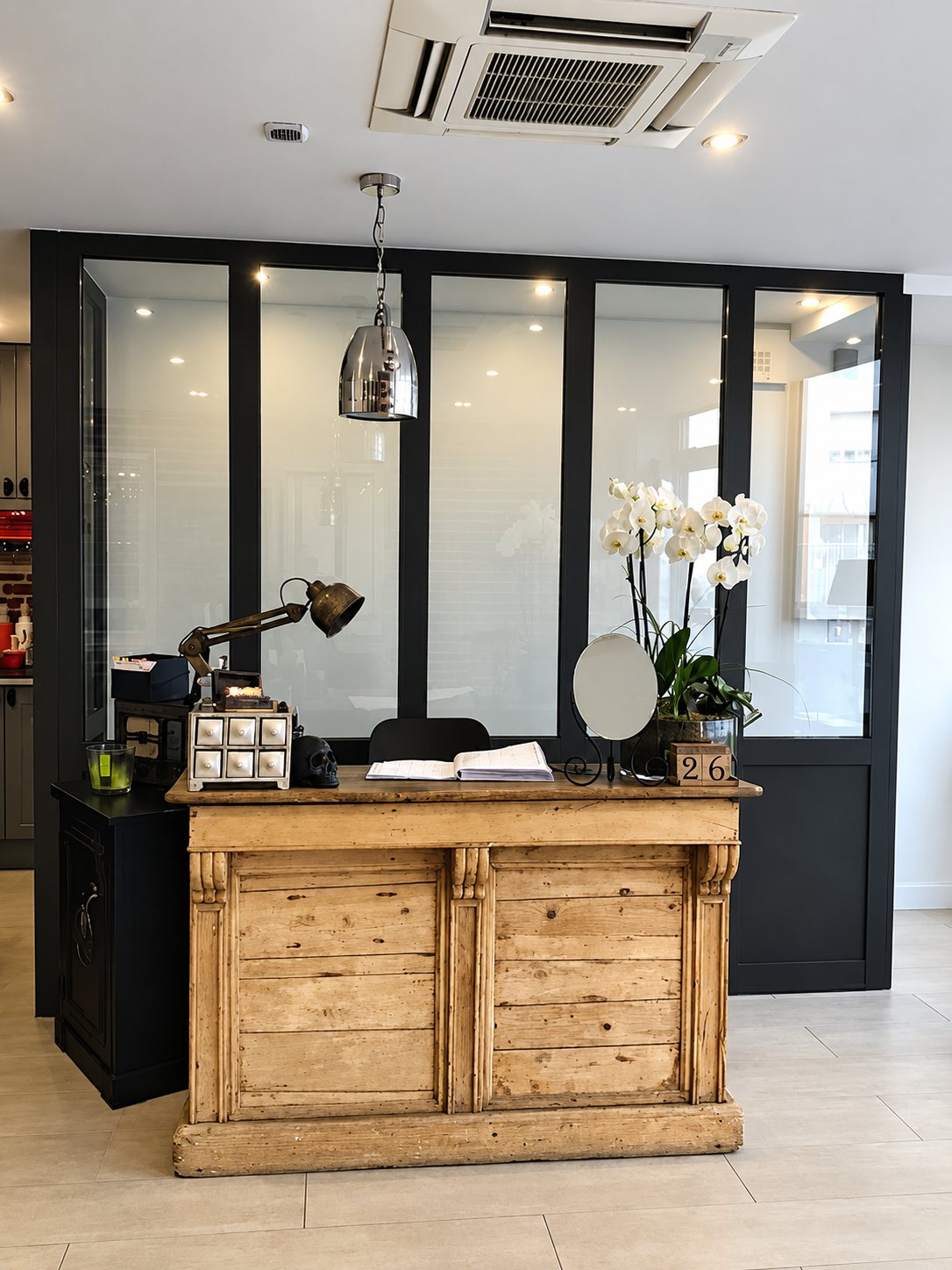Comptoir d’accueil en bois ancien, orchidée blanche et verrière noire.