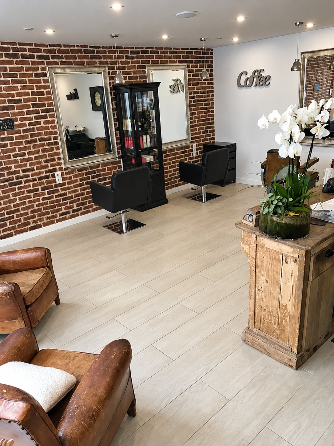 Vue du salon depuis les fauteuils en cuir : orchidées blanches sur un meuble en bois et mur de briques.