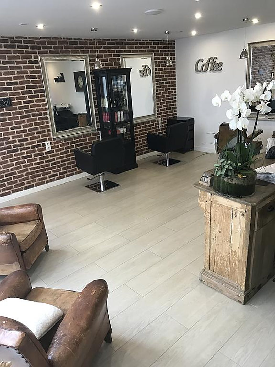 Salon de coiffure lumineux : mur de briques, miroirs, fauteuils noirs et fauteuils en cuir vieilli.